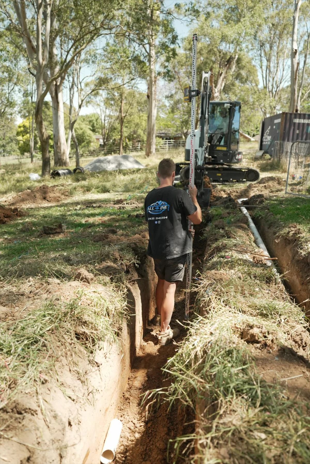 A plumber measuring pipework in an open trench