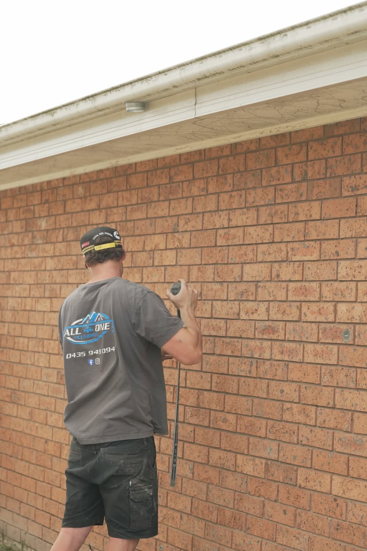 Josh up a ladder clearing gutters on a brick home